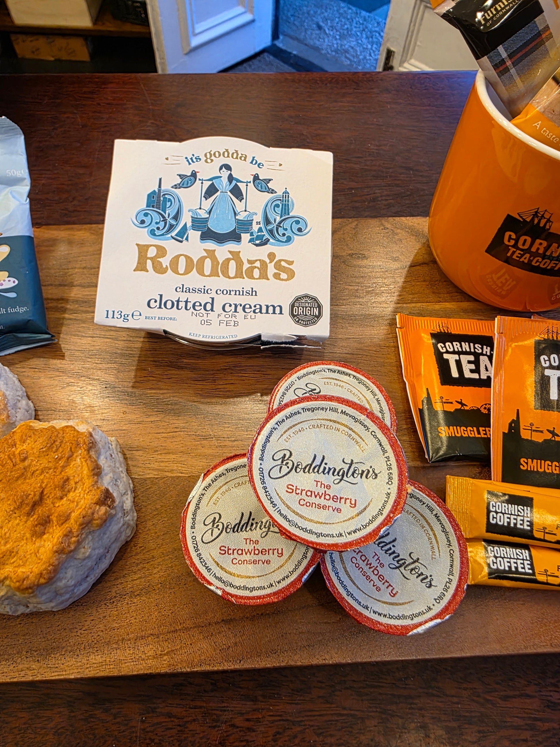Assorted food items including coffee, clotted cream, and a jar of mustard on a wooden surface.