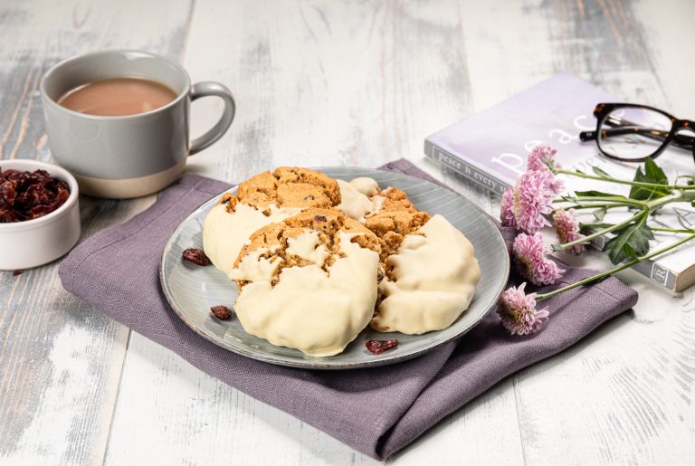 Plate of cookies with a cup of coffee, raisins, and flowers on a wooden table.