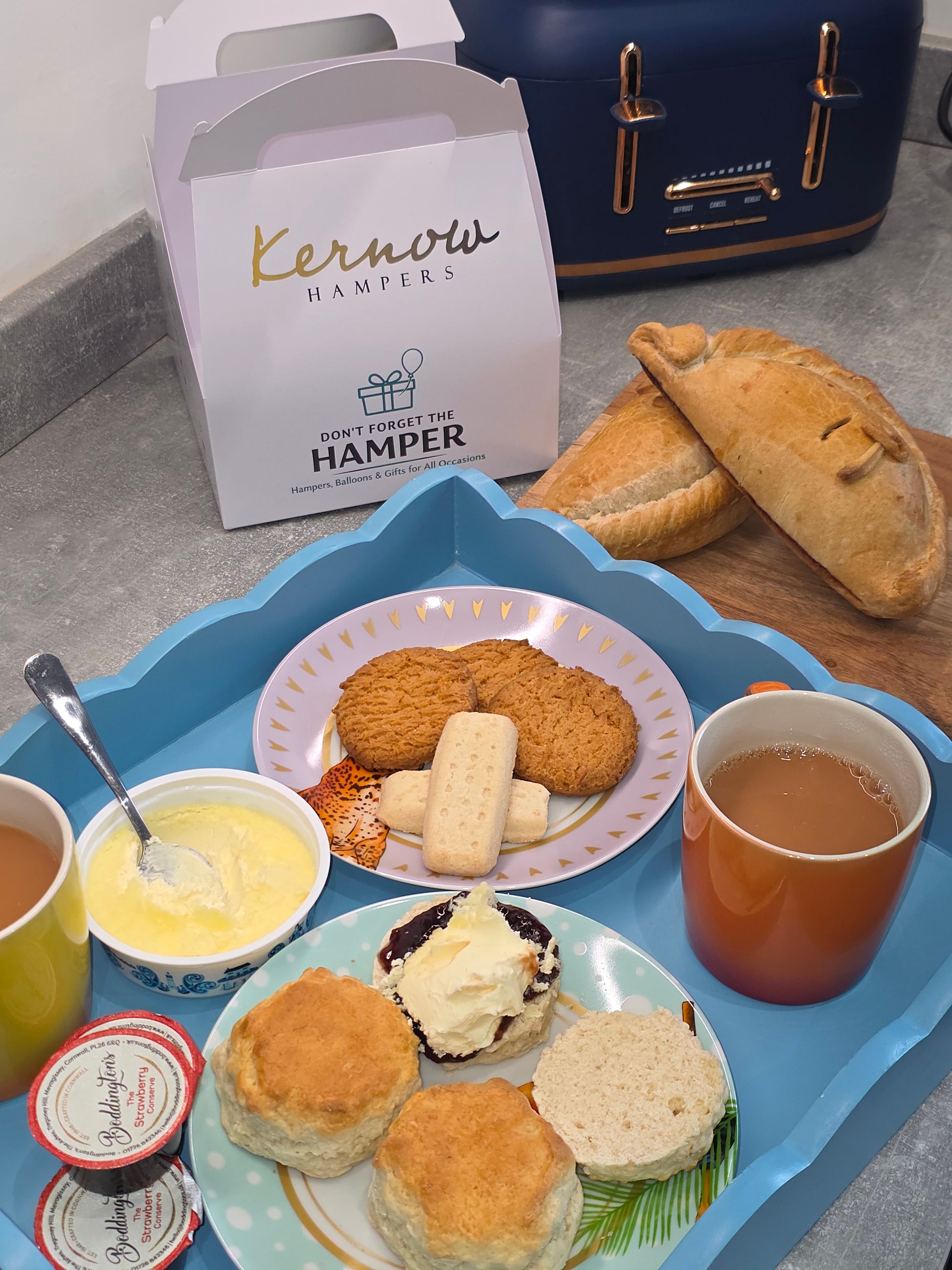 Tea time set with scones with jam and clotted cream on top, cookies, and tea on a blue tray.