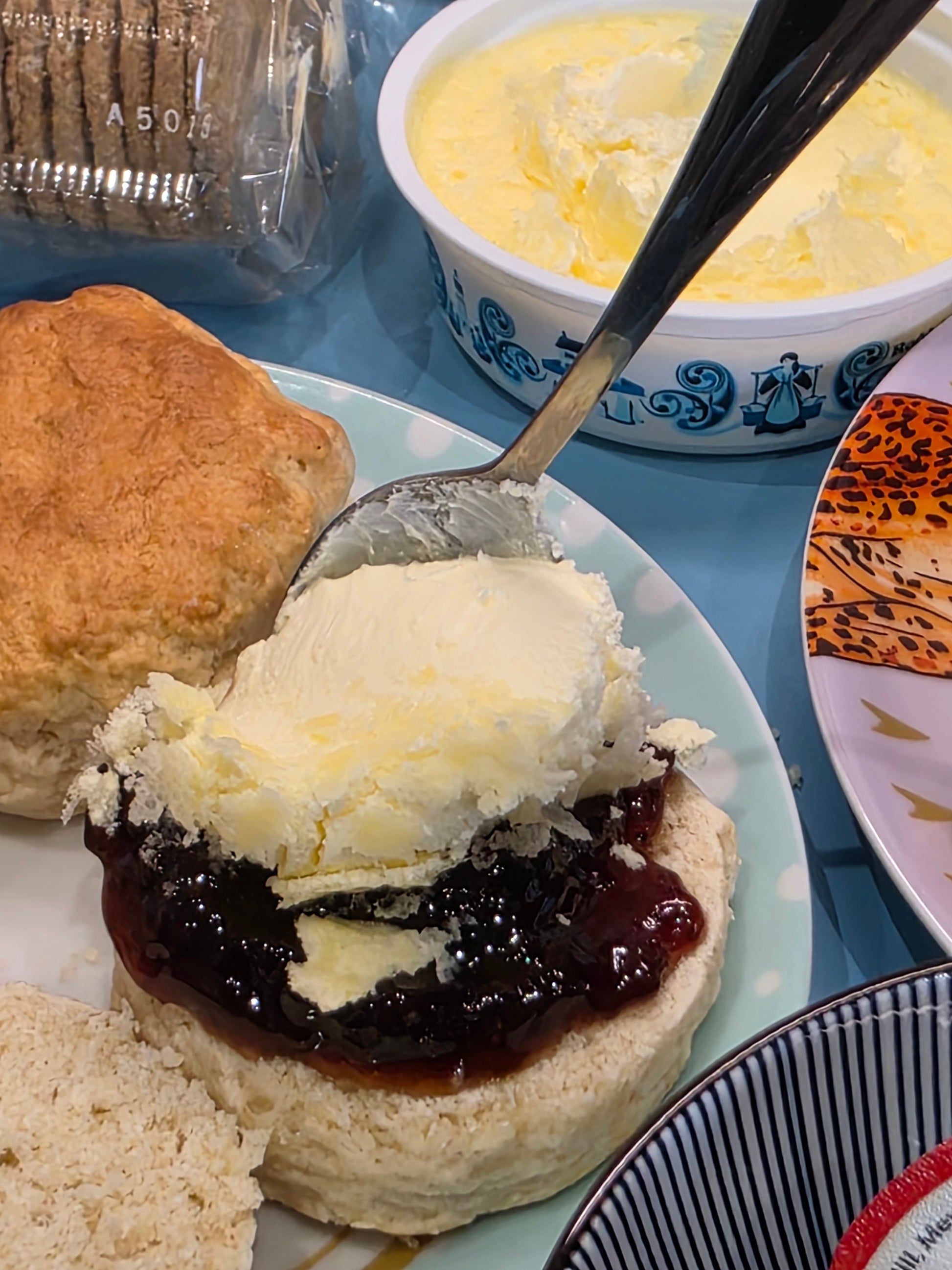 Scone with jam first and clotted cream biscuit with surrounded by other dishes and a packet of biscuits.