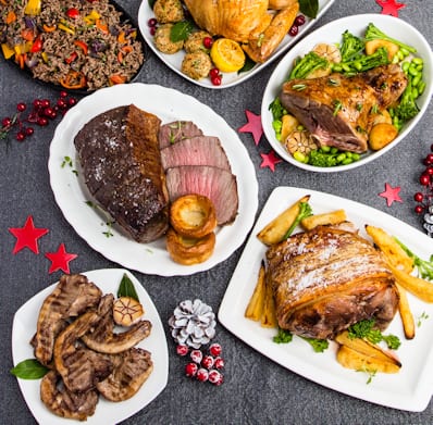 Assorted roasted meats and vegetables on white plates with a dark background