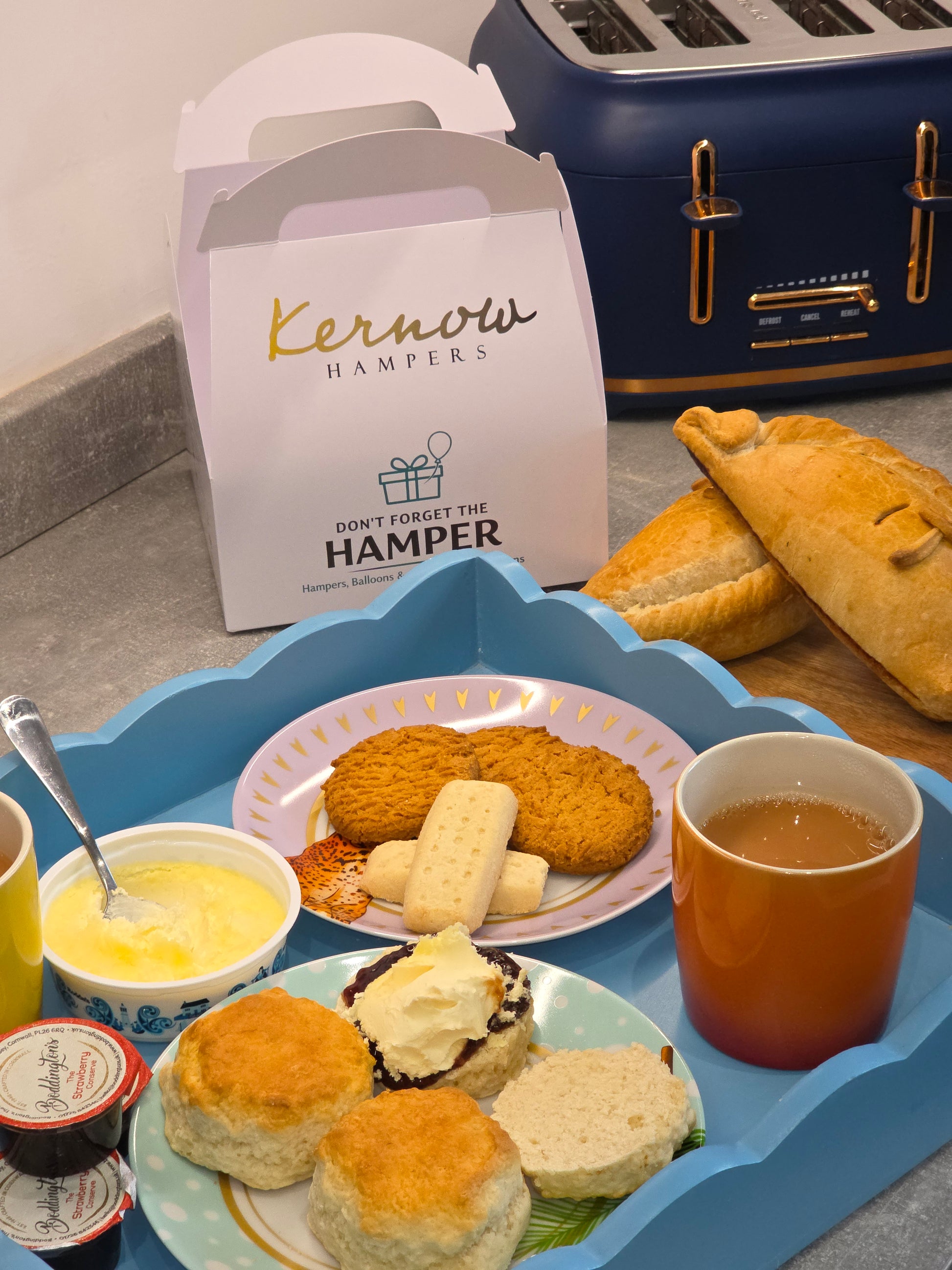 Assorted food items including pastries, a cup of tea, and a box labeled 'Kerryn's Hamper' on a table.