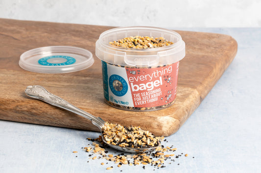 Container of everything bagel seasoning with a spoonful on a wooden board