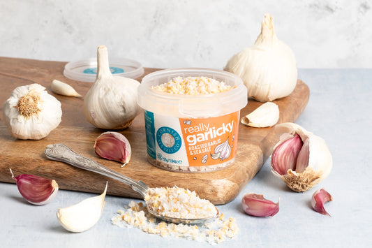 Container of 'really garlicky' spread with garlic bulbs and cloves on a wooden board.